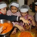 Des enfants équipés de charlottes mélangent des carottes rapées avec d'autres ingrédients pour préparer des cakes aux carottes