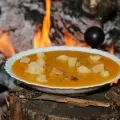 Une assiette creuse avec une soupe orangée et des croutons de pain est présentée devant un feu de cheminée allumé