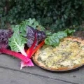 Une tarte aux blettes ainsi qu'un bouquet de blettes sont posés sur une table en bois