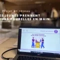 Un ordinateur portable ouvert permettant de voir la page de présentation du projet réseau "Les jeunes prennent leurs poubelles en main" contenant une illustration de poubelle de recyclage avec 2 personnes qui viennent trier leur déchet