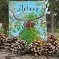 Le livre Arbres est exposé sur un grand tronc coupé et entouré de pommes de pin