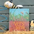 Le livre Abeilles et vers de terre est présenté face couverture, appuyé contre un composteur et entouré de deux peluches en forme d'abeilles