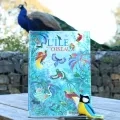 L'album L'ile aux oiseaux est présenté sur une table de pique-nique et un paon apparaît sur le muret en arrière plan