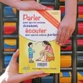 Le livre est présenté face première de couverture, maintenu par trois mains d'enfants 
