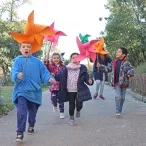 un goupe d'enfants et leur animatrice courent avec un grand moulin à vent en papier dans la main