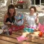 Une animatrice colle avec un enfant un éléments naturel et deux autres enfants nous montrent leurs œuvres