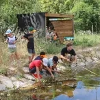 une groupe d'enfants et leur animatrice sont accroupis devant une mare
