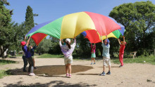 des enfants jouent en tenant chacun un bout d'une toile de parachute : un jeu cooperatif