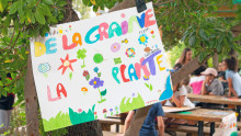 Un panneau réalisé par les enfants en premier plan avec écrit : de la graine à la plante et des enfants floutés en arrière plan