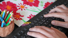 Des main tapent sur un clavier d'ordinateur entouré de crayons de couleur et d'un dessin d'enfant