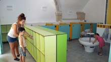 Un enfant accompagné d'un animateur récupère des affaires dans son casier pendant que deux autres boivent à la fontaine des nouveaux sanitaires du centre maternel