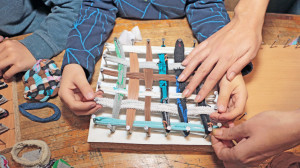 Des mains d'enfants et d"adulte en gros plan tendent des morceaux de tissus sur une planche en bois cloutée pour fabriquer un tawashi