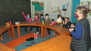 Une adulte anime en salle un atelier philo sur la solidarité face à un groupe d'enfants