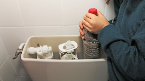 Un enfant place une bouteille en plastique remplie de sable dans le réservoir des toilettes pour économiser de l'eau