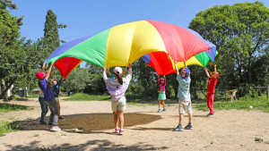 Des enfants jouent au jeu du parachute, une grande toile de couleurs qui est déployée en coopérant