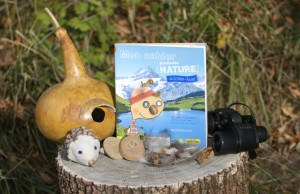 Livre "Mon cahier d'activités nature automne hiver" sur un tronc coupé avec des créations nature et une paire de jumelles