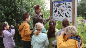 Une animatrice montre aux enfants munis de jumelles un panneau représentant les oiseaux de notre région