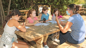 4 jeunes filles interrogent la directrice de l'Accueil de loisirs sur une table de pique-nique